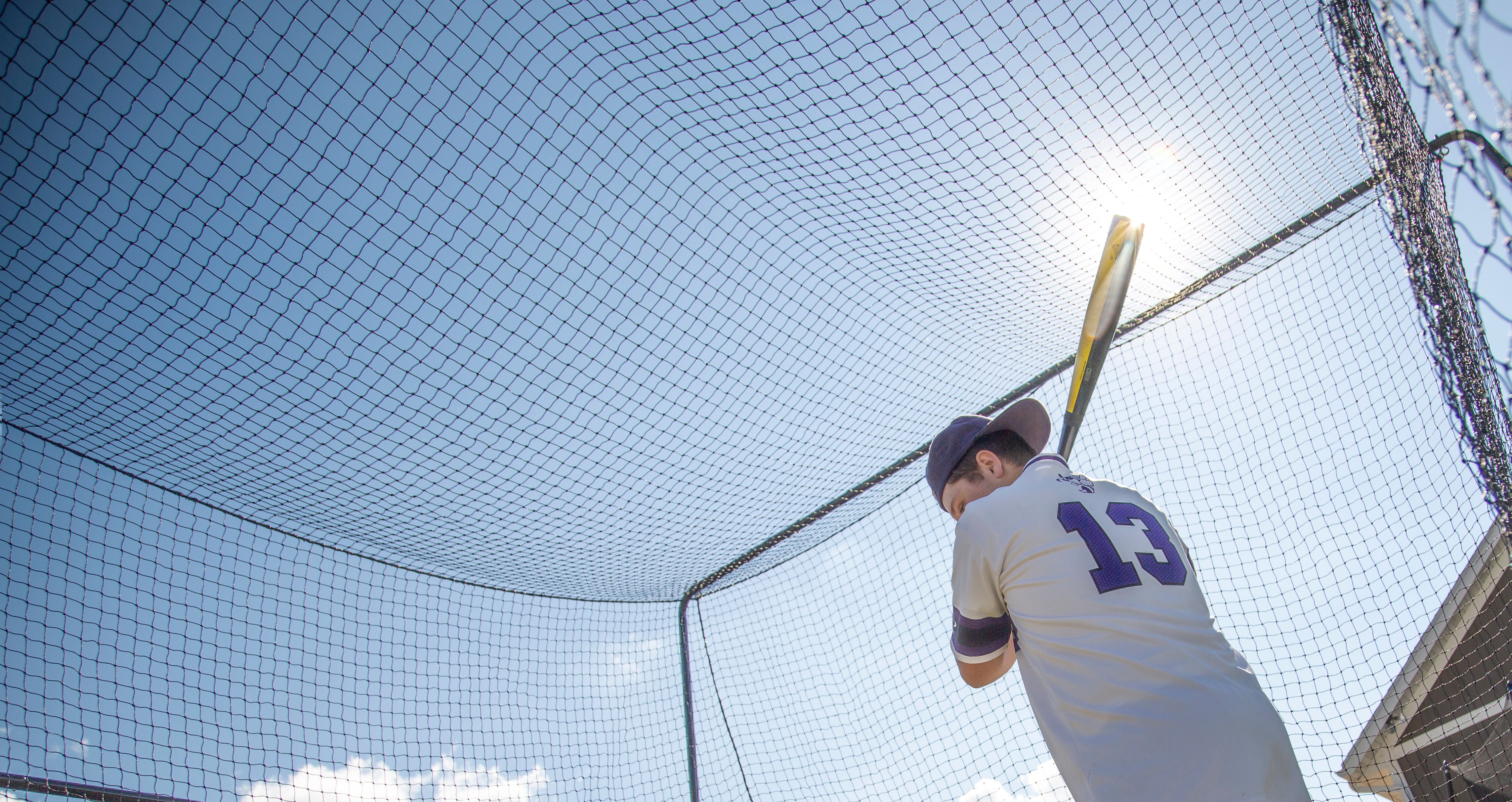 A young man swinging his baseball bat inside of the batting cage. 