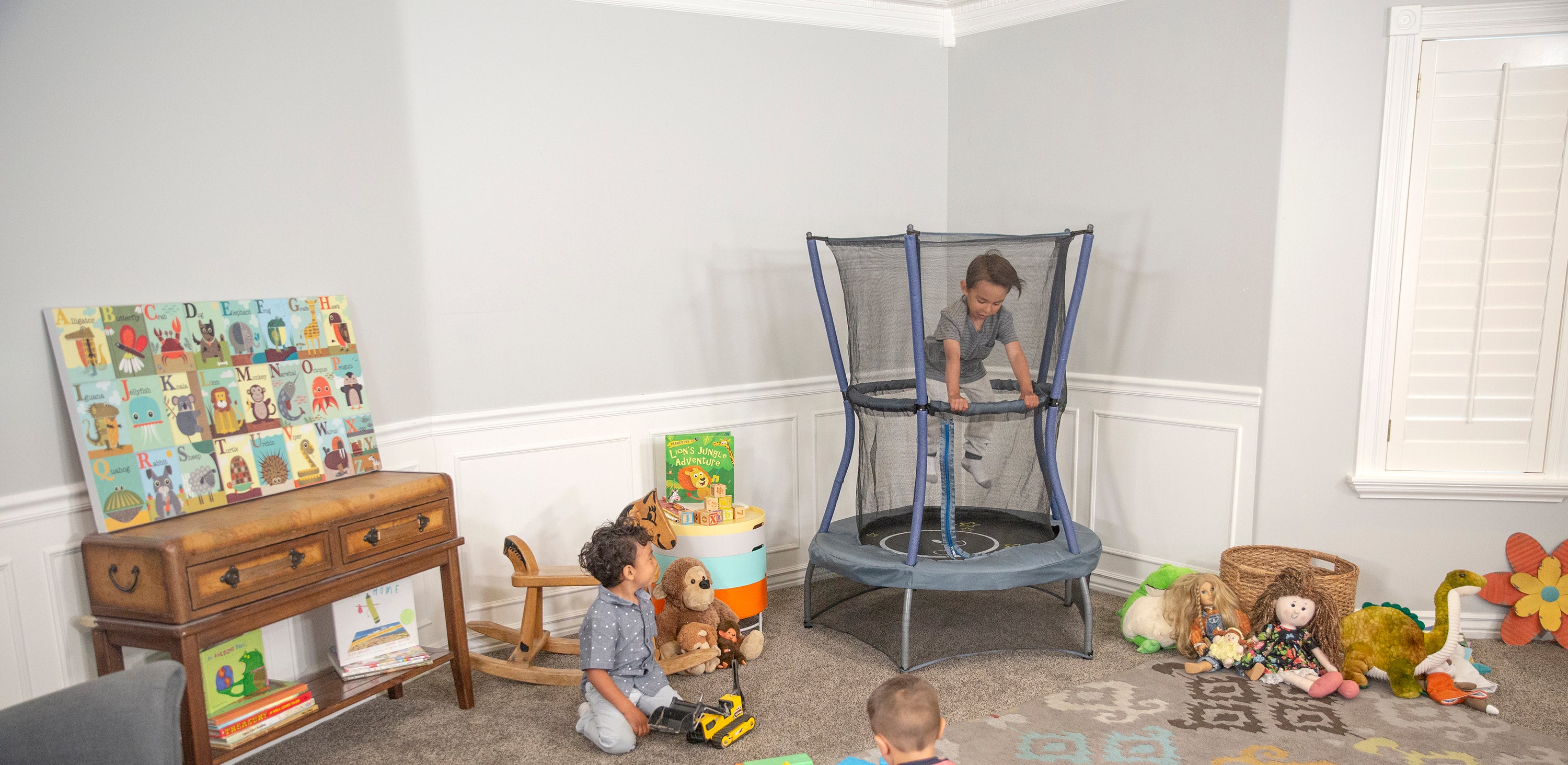 Two young boys are playing with a yellow and gray mini trampoline. 