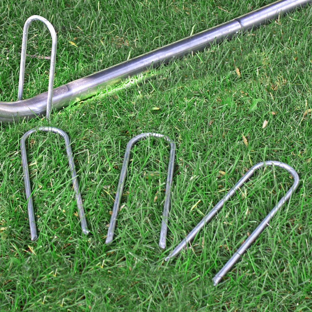 One wind stake is placed on top of the trampoline leg while three other wind stakes lay in the grass.