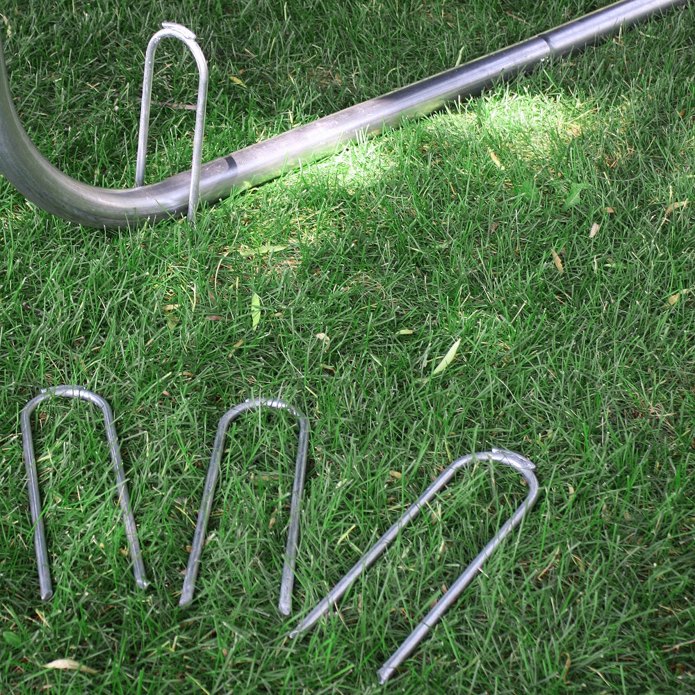 Three trampoline wind stakes laying in the grass while one wind stake is put on top of the trampoline leg. 