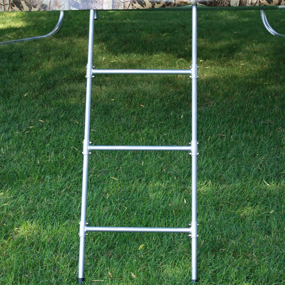 Trampoline sitting in grass yard with trampoline ladder hooked on it. 