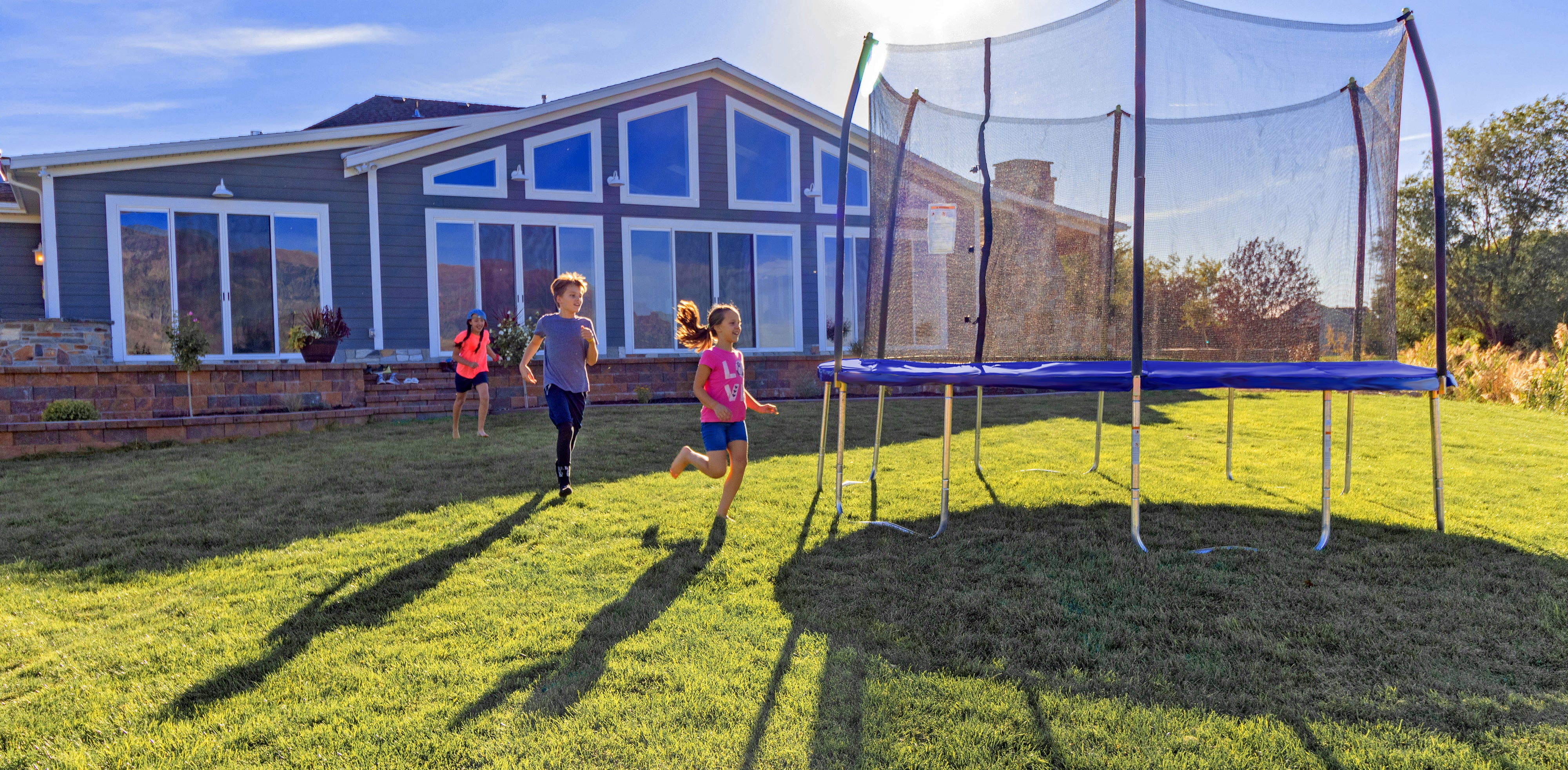 A group of children running across the yard towards a trampoline. 