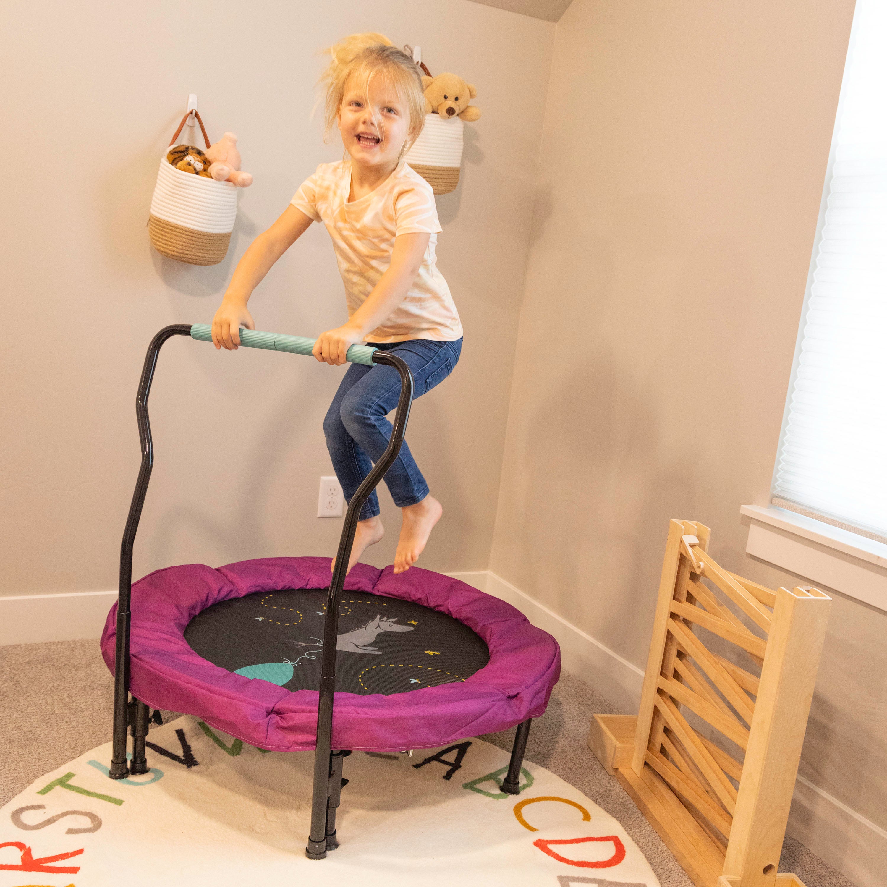 The 36” Eeyore toddler trampoline sits in the corner of a room while a young girl jumps on it. 