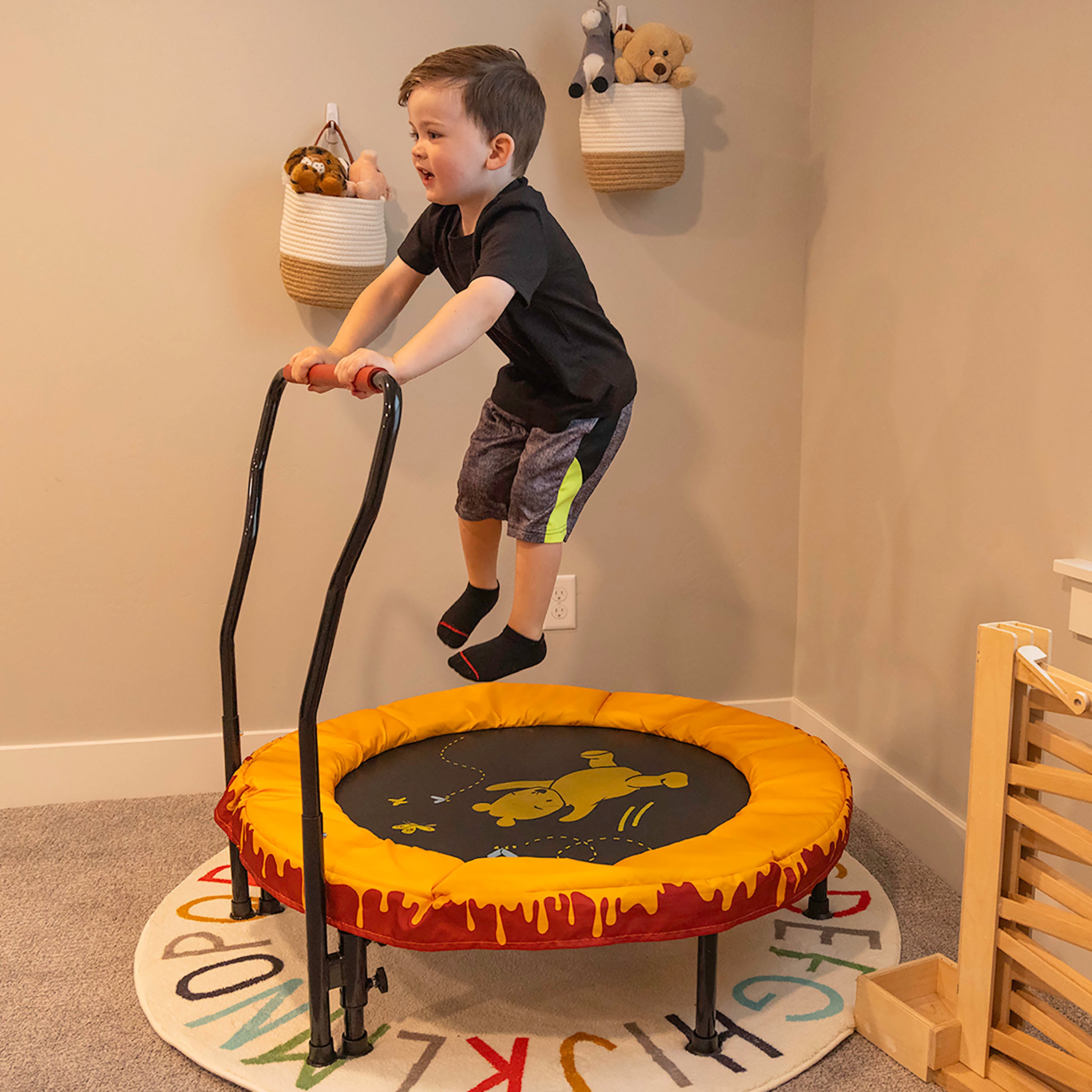 A little boy jumps high on the 36” Winnie the Pooh trampoline while it sits in the corner of the playroom. 