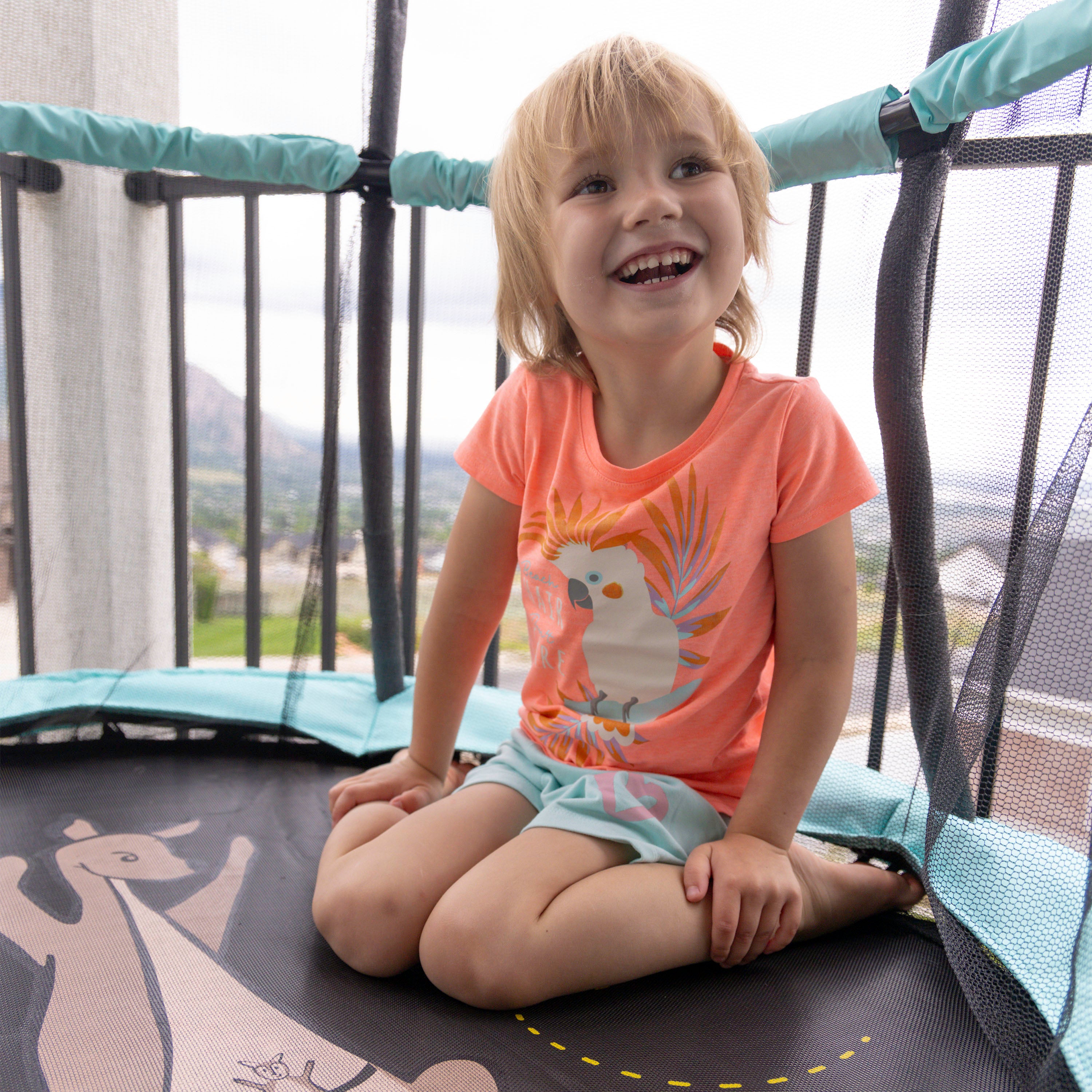 A little girl sits on the jump mat of her Kanga & Roo trampoline. 
