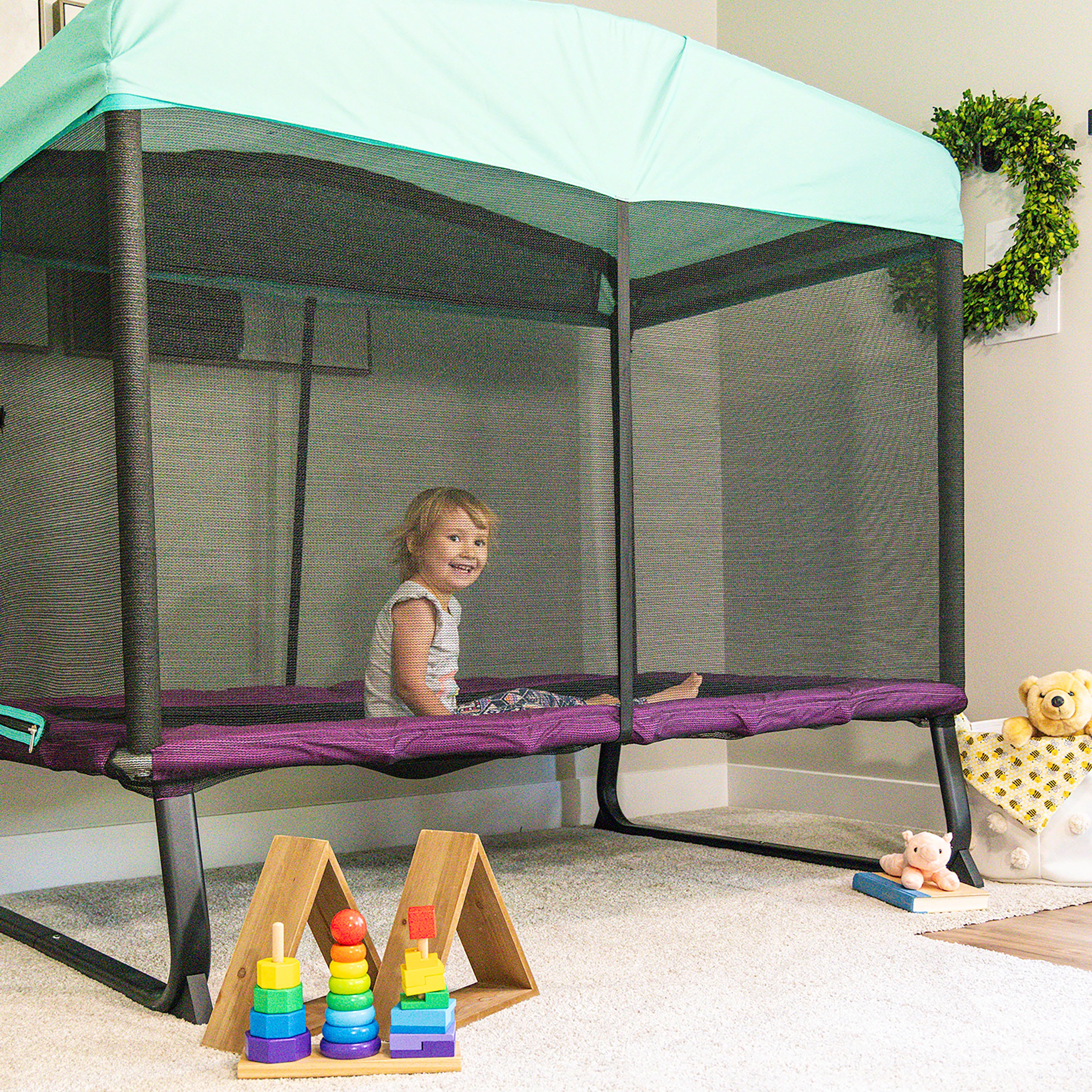 The rectangle Eeyore trampoline sits in the corner of a playroom. A young girl sits happily on the trampoline. 