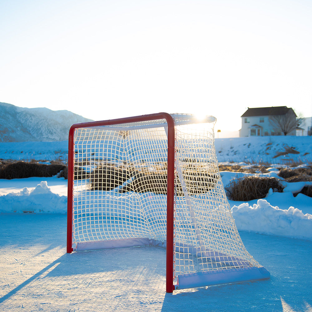 The sun shines on the hockey goal with ice and snow in the background. 