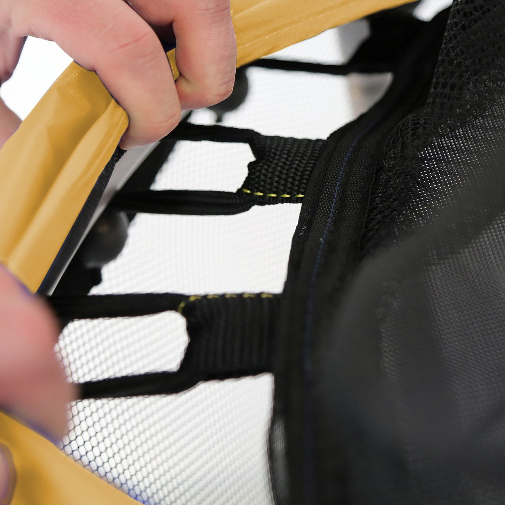 Fingers pull back the yellowish-orange frame pad to reveal stretch cords attached to black jump mat. 