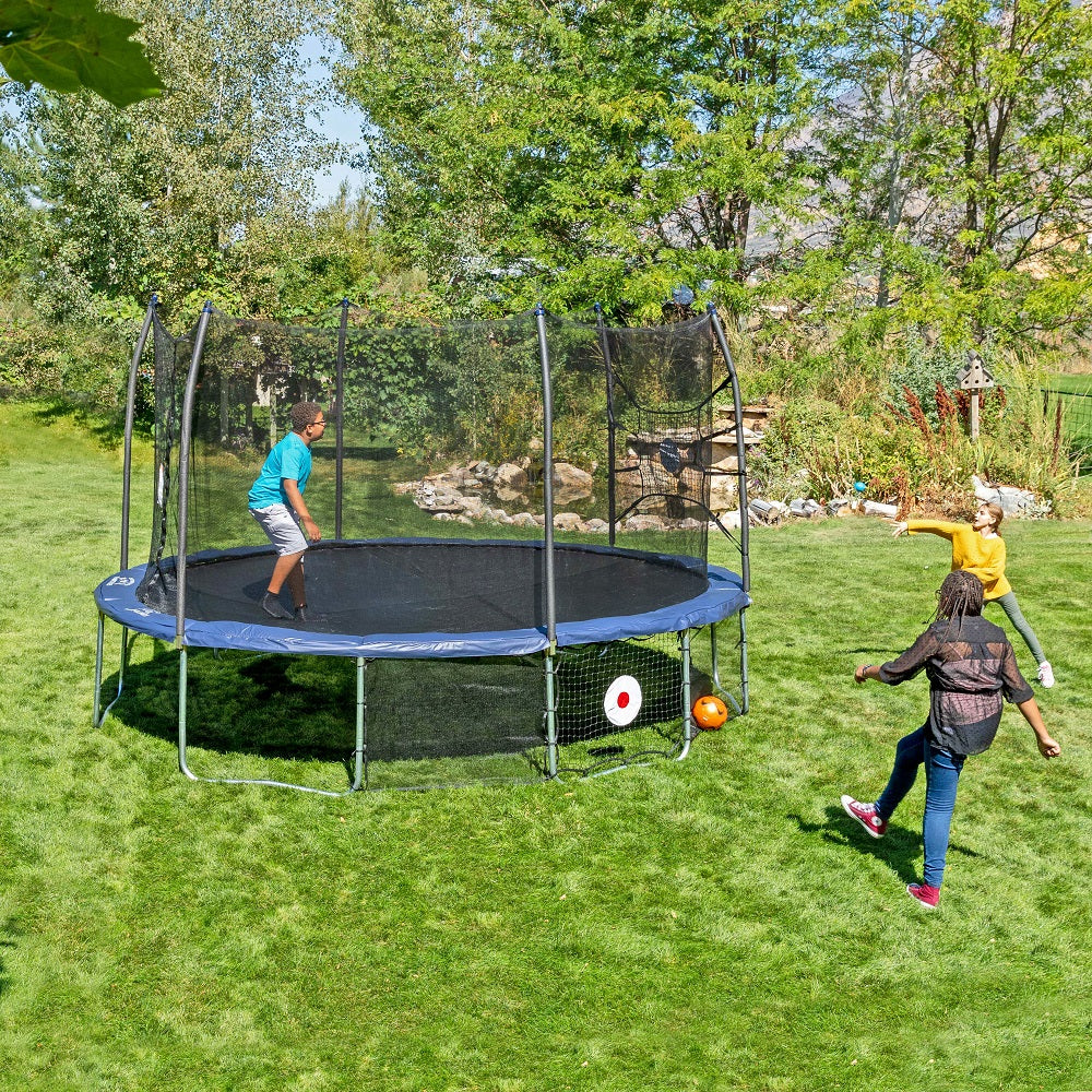A boy jumps on the trampoline while two girls play with the Kickback and Bounceback nets. 
