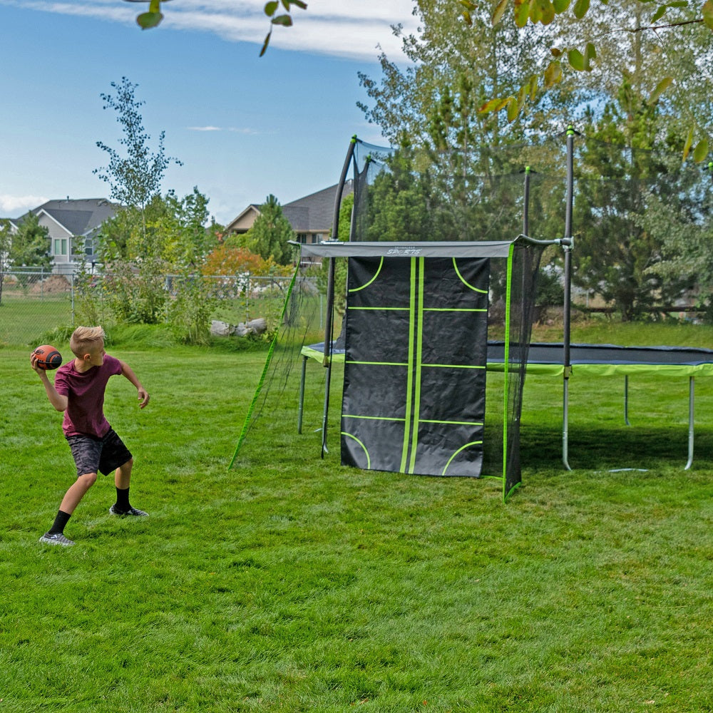 Boy pulling back arm to throw football at the sports net trampoline accessory. 
