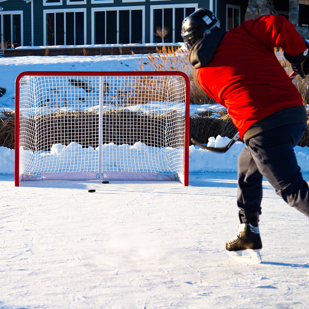 A man skating on ice hits the hockey puck into the hockey goal. 