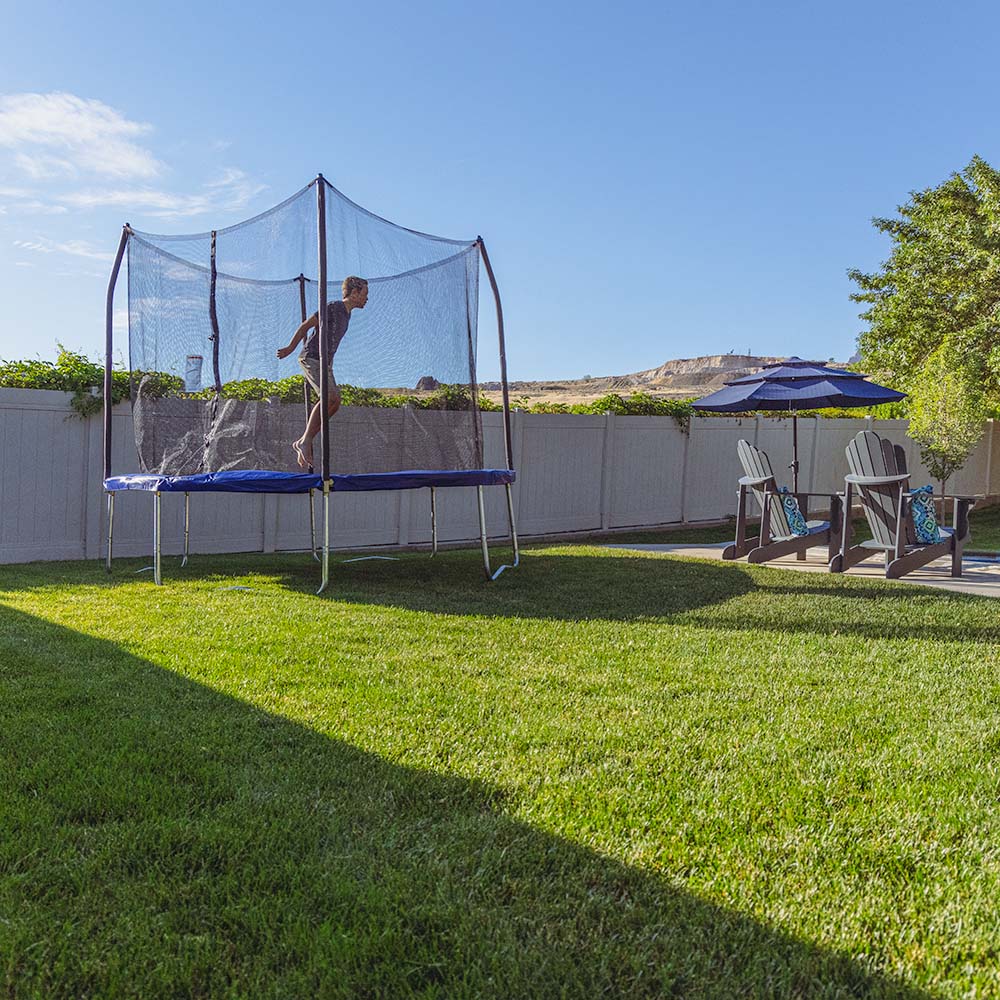 A boy jumps on the blue 10-foot trampoline in a sunny backyard area. 