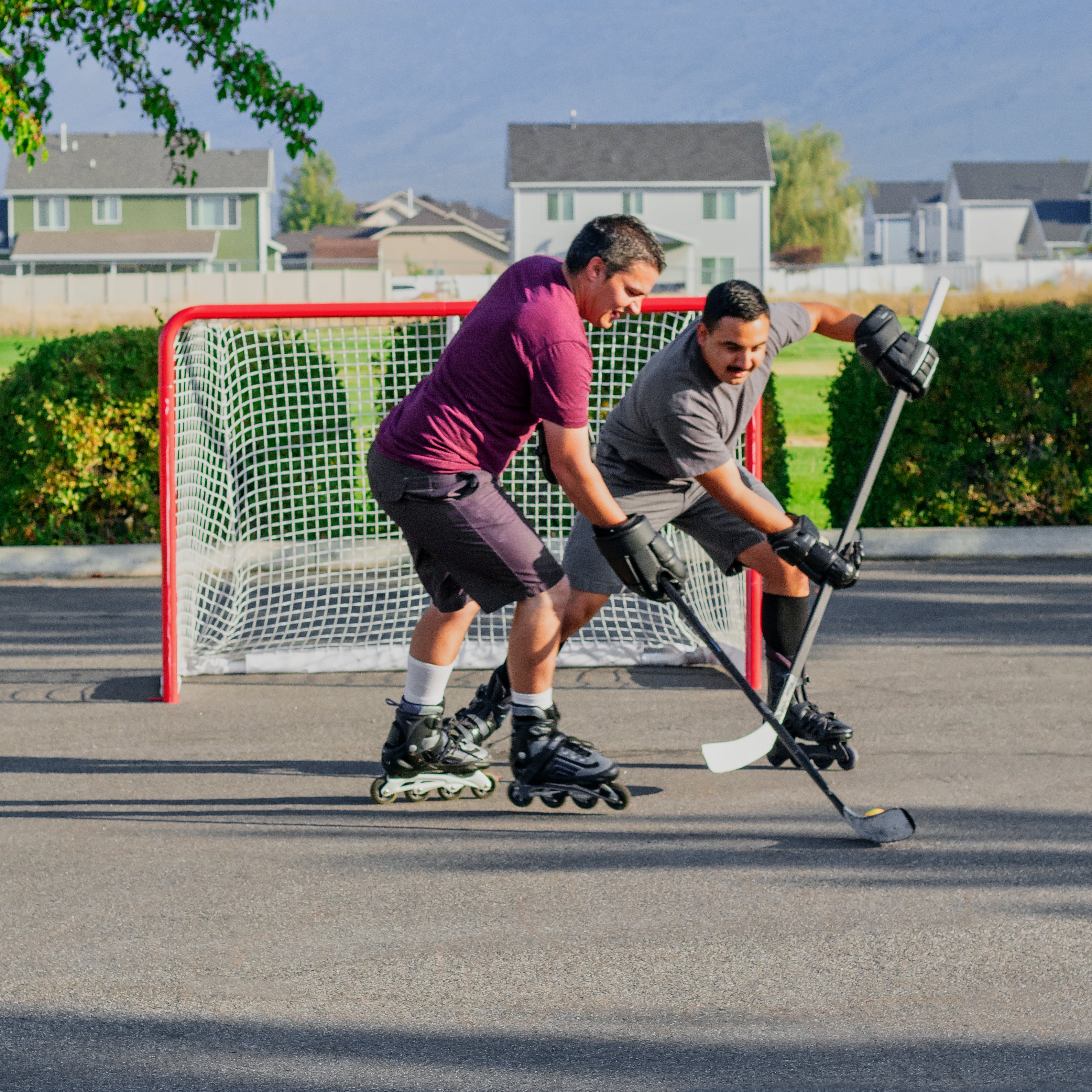 Two men in roller blades play street hockey with the hockey goal.