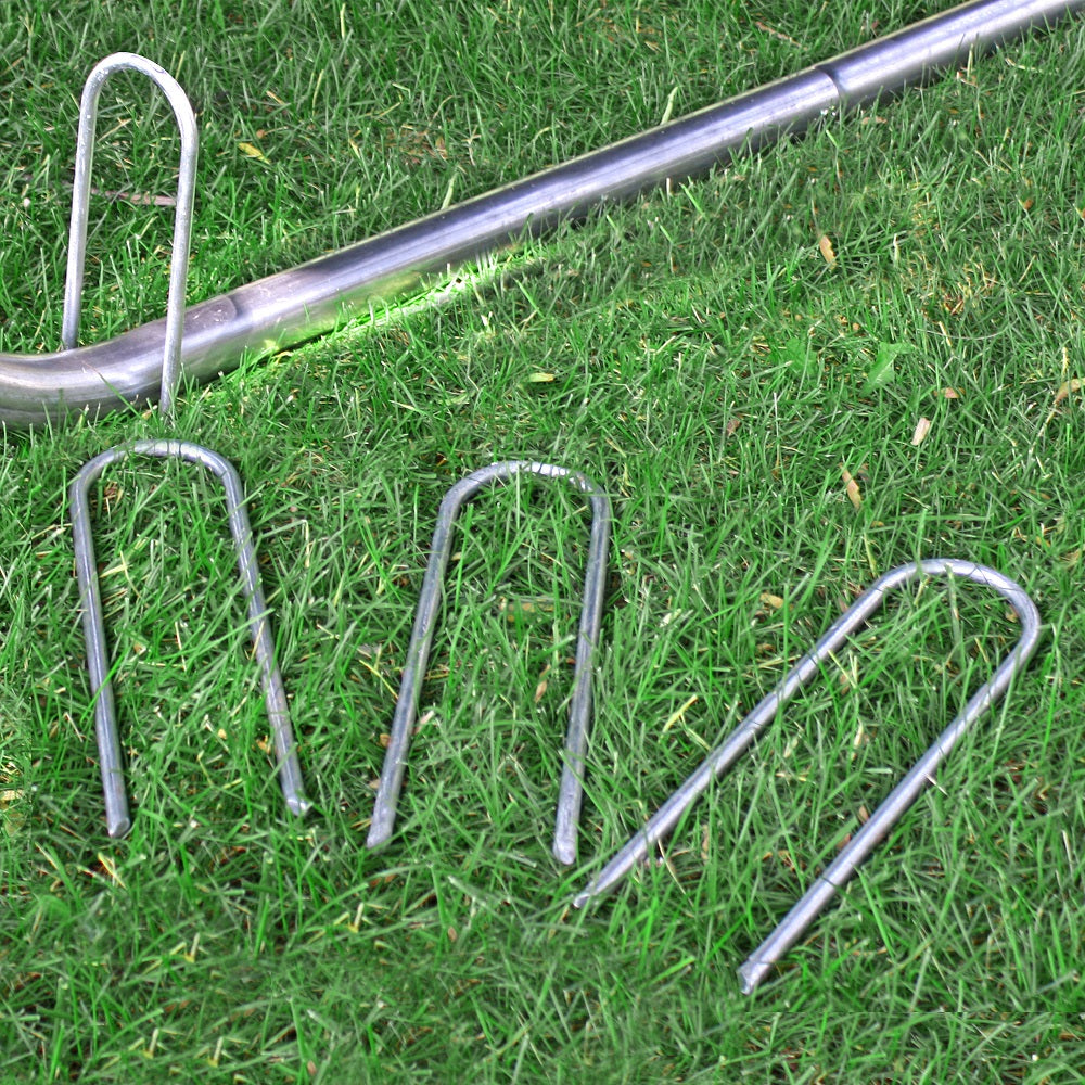 One wind stake is placed on top of the trampoline leg while three other wind stakes lay in the grass. 