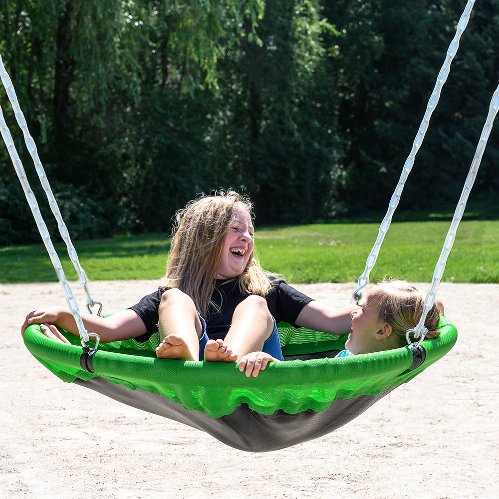 Two young girls sit together in the saucer swing seat. They are looking at each other and laughing. 