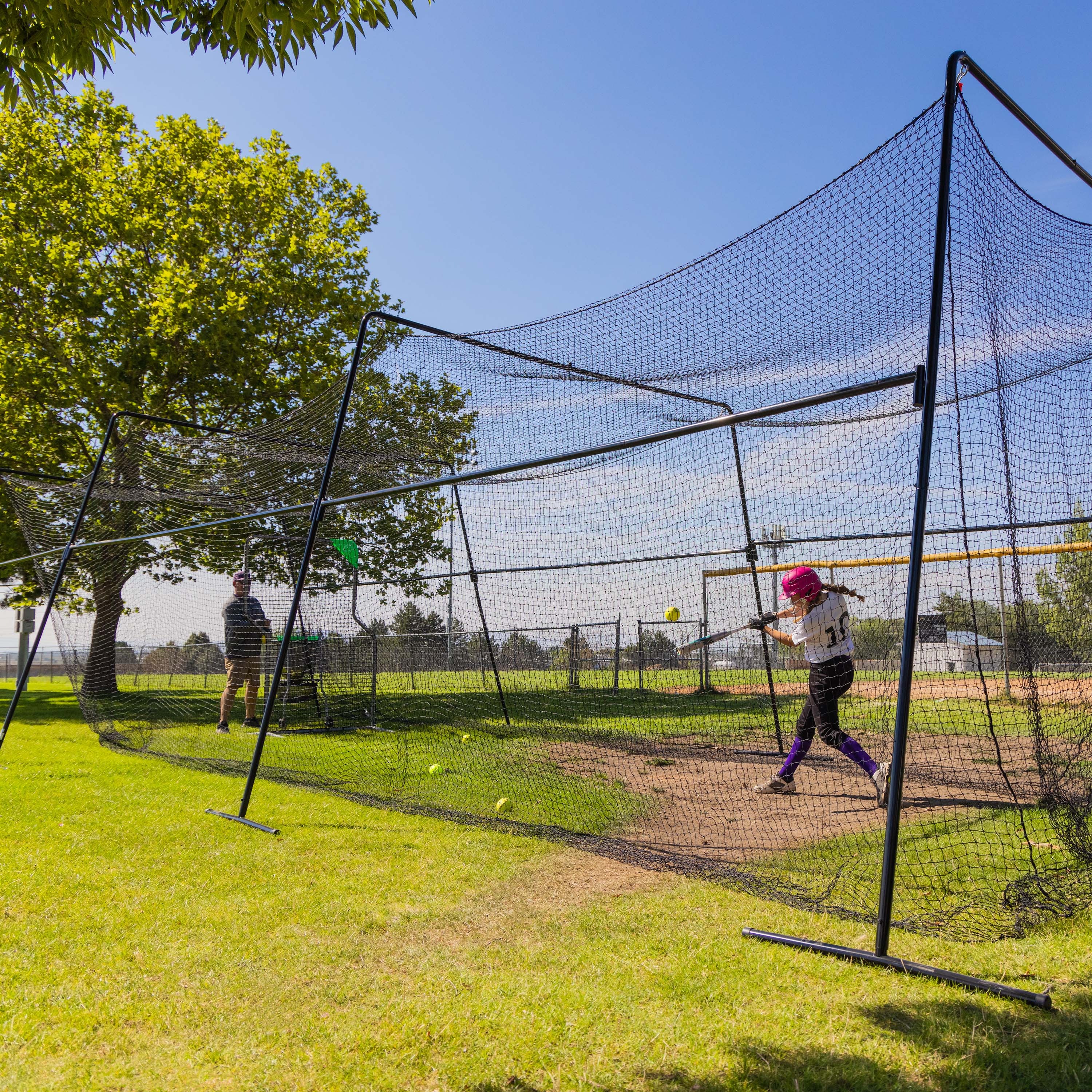 A coach and a softball player practice batting in the batting cage.