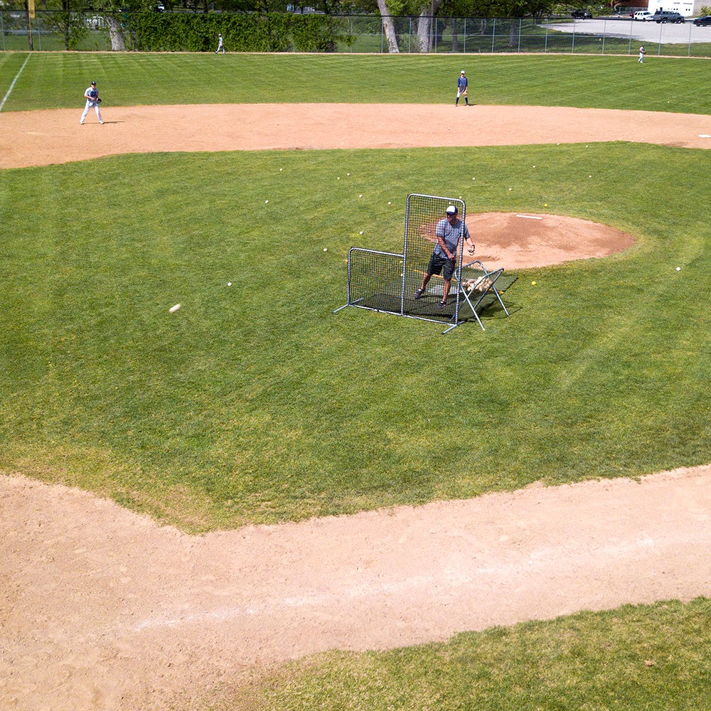A coach uses the Pitchers L-Screen for protection on the baseball field. 