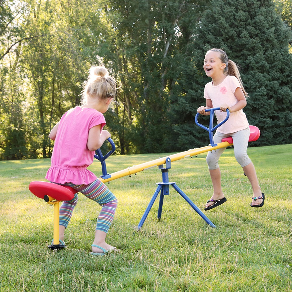 Two young girls teetering on the red, yellow, and blue swivel Teeter Totter. 