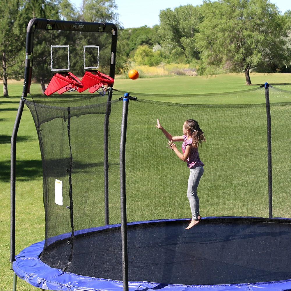 A little girl shoots the basketball while jumping on the trampoline. 
