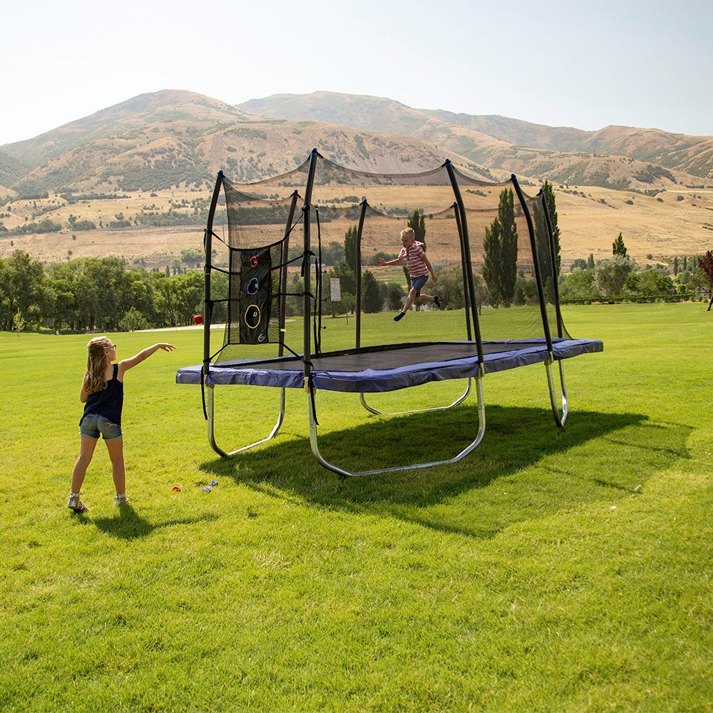 A girl throws a bean bag at the Triple Toss Game while a young boy jumps on the trampoline. 