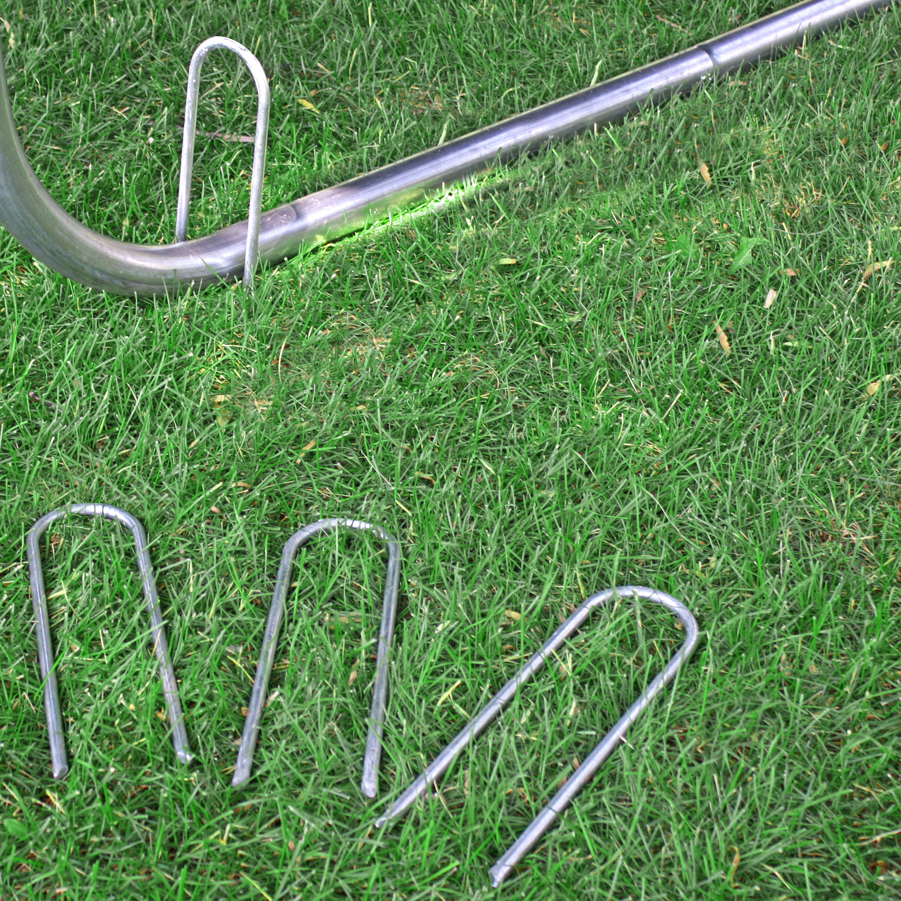Three wind stakes lay on the grass while one wind stake is placed over the trampoline leg. 