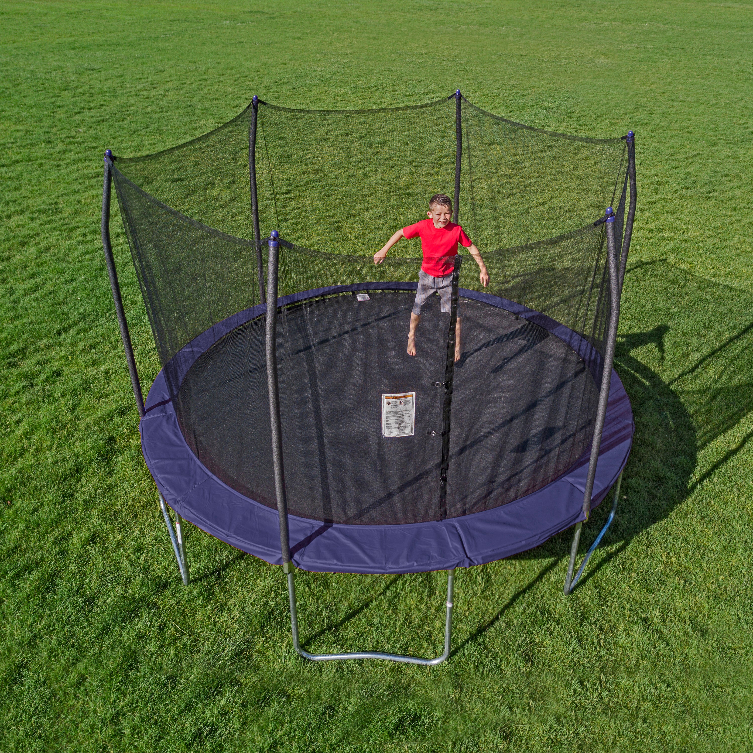 Young boy grins while bouncing on the 13-foot round trampoline with navy spring pad.