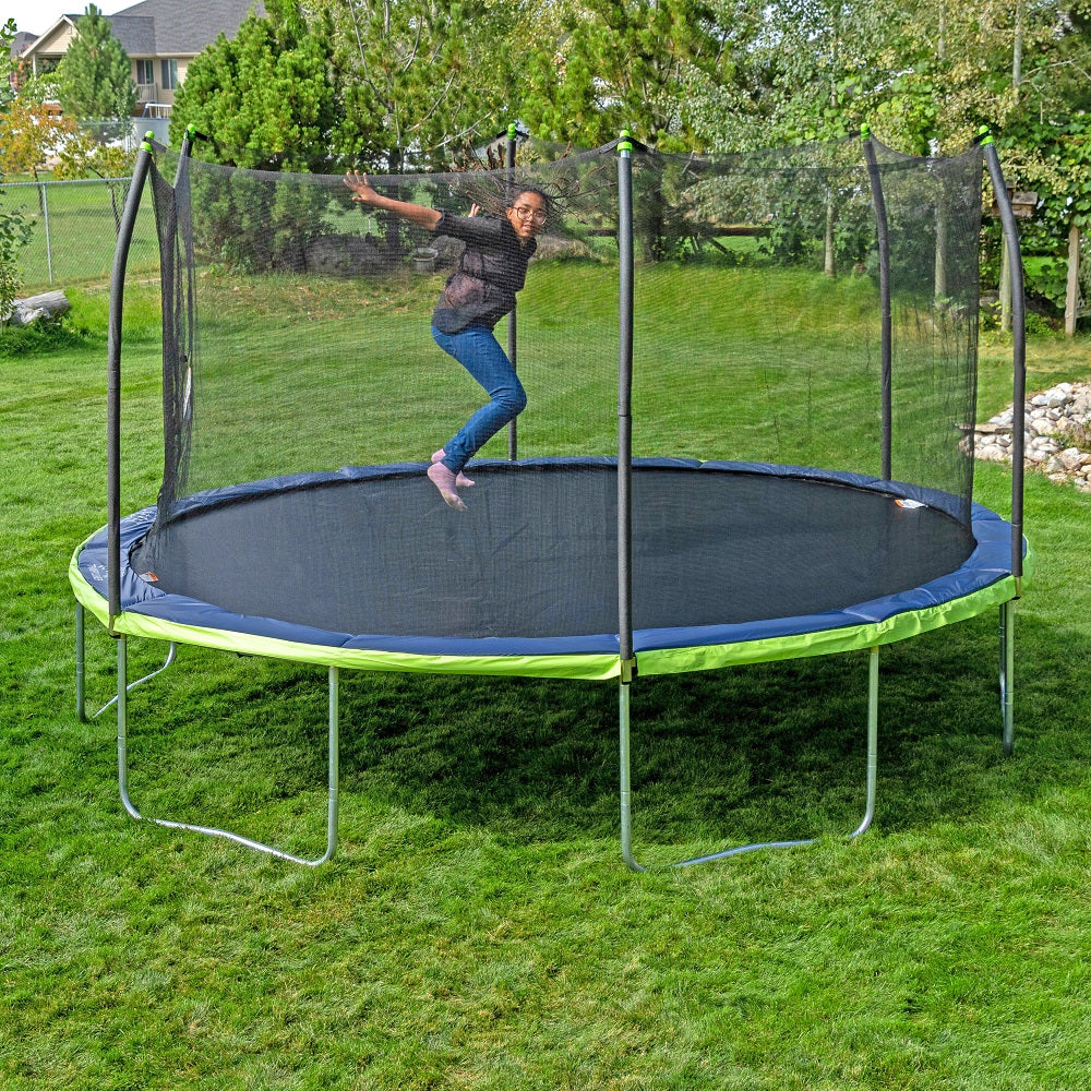 Teenage girl jumps on the 15-foot oval trampoline with dual color spring pad and lime green pole caps. 