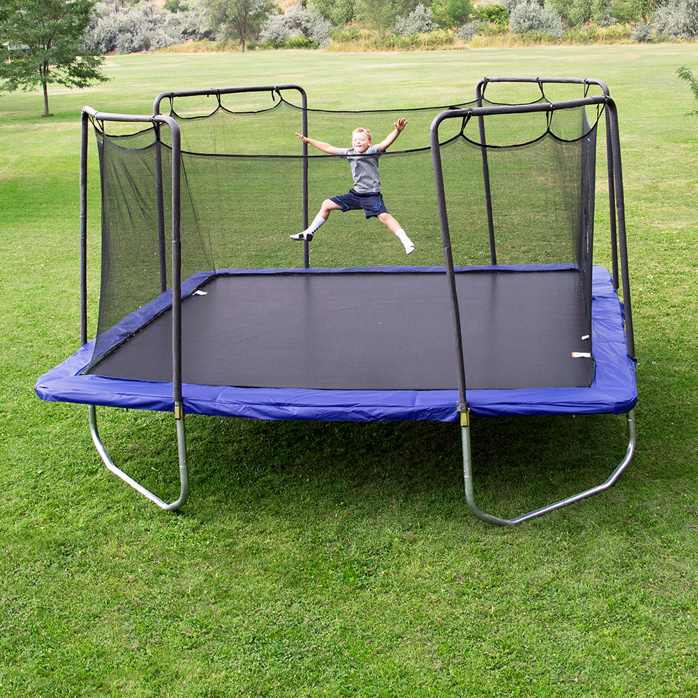 Young boy jumps with arms wide on 15 foot square trampoline with blue spring pad. 
