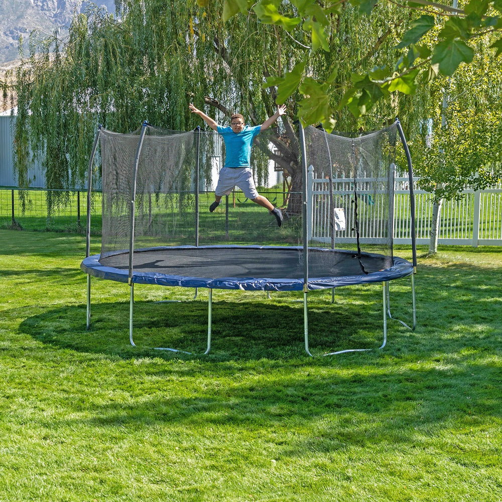 Teenage boy jumps with limbs wide on the 15-foot oval kids trampoline with navy spring pad and navy pole caps. 