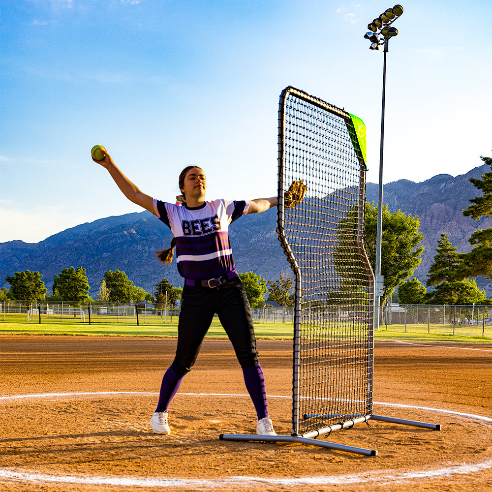 A softball player pitches while standing behind the Z-shaped screen. 